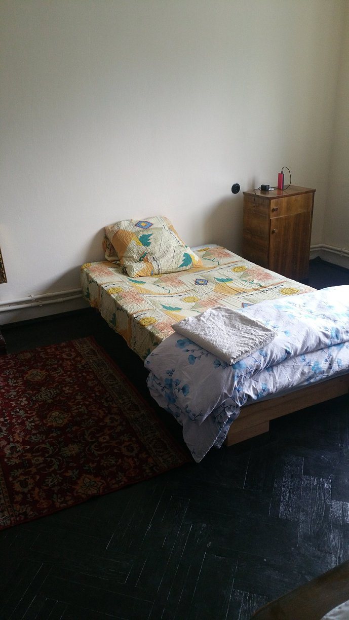 Dormitorul casei cu pat single si covorase pe parchet
